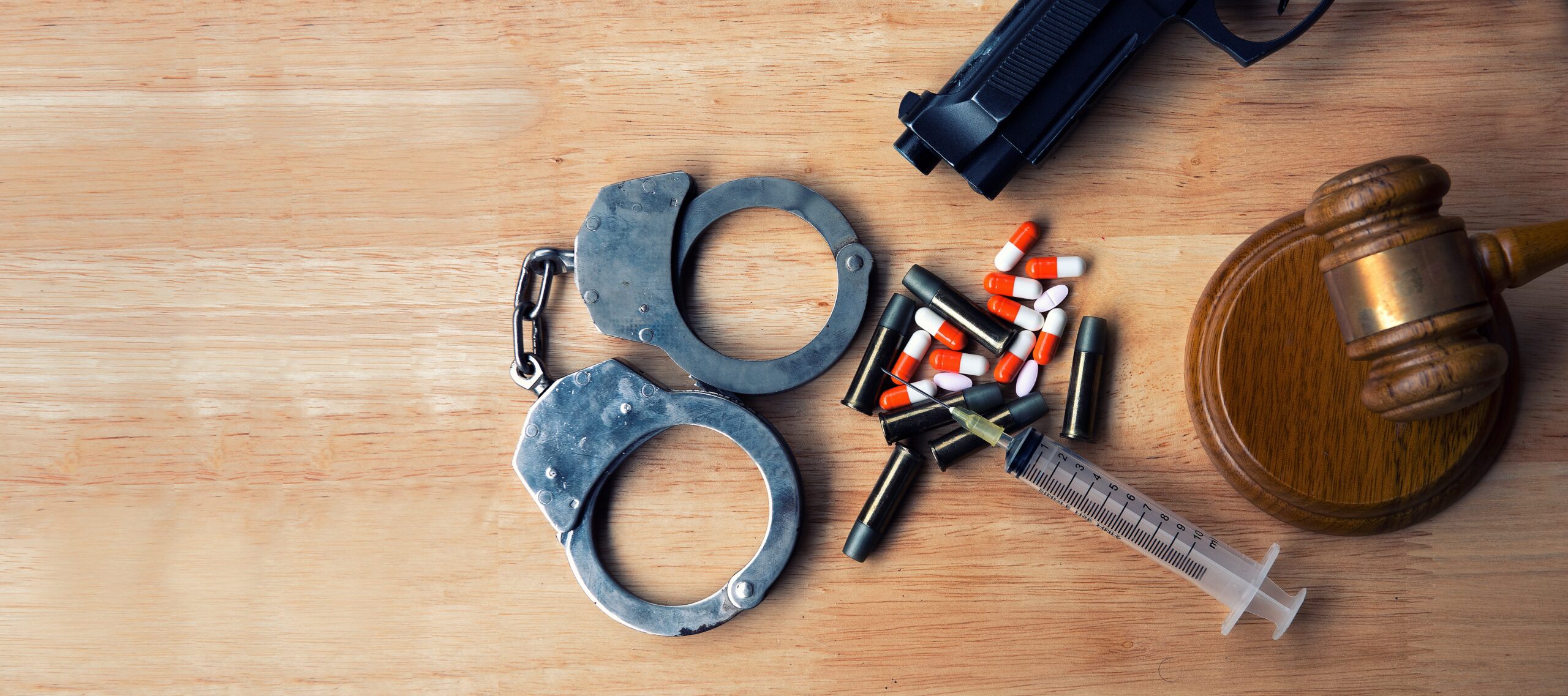 Drugs, a gun, bullets, handcuffs, and a justice gavel are scattered together on a wooden background. If you’ve been charged for a serious drug crime, contact our experienced Oklahoma drug lawyer.